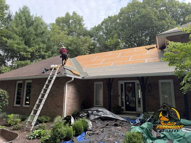 brick house exterior with roofer on roof and ladder against wall - Exterior work, home in progress, Avon, CT
