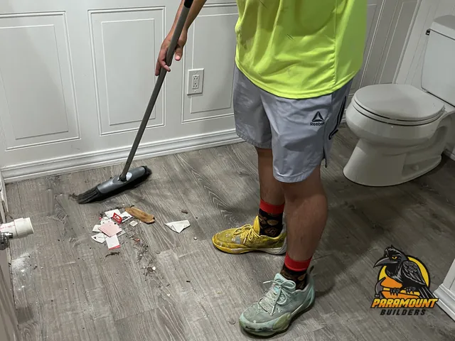 Crew member sweeping debris from gray plank bathroom floor near wainscoting - Water damage restoration, home in progress, East Hartford, CT